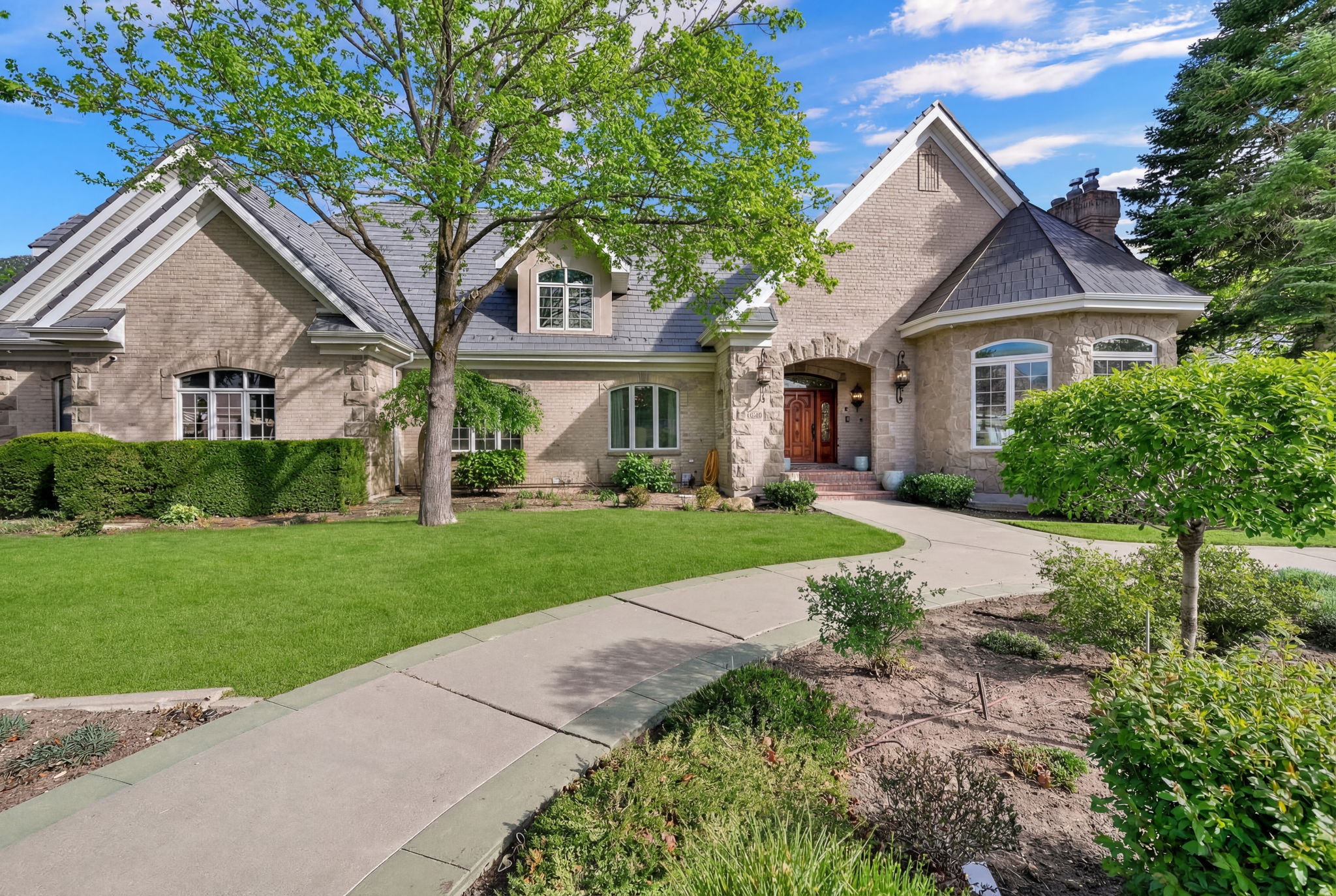 Summer exterior of the Orem estate with mature landscaping, stone exterior, and curved approach