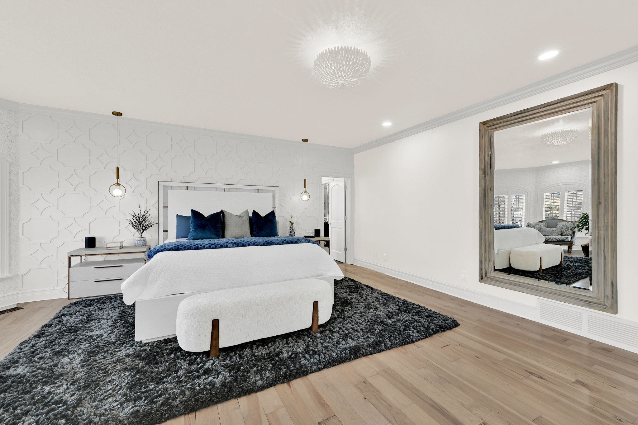 Primary bedroom with wide bed, large mirror, white walls, and warm wood flooring