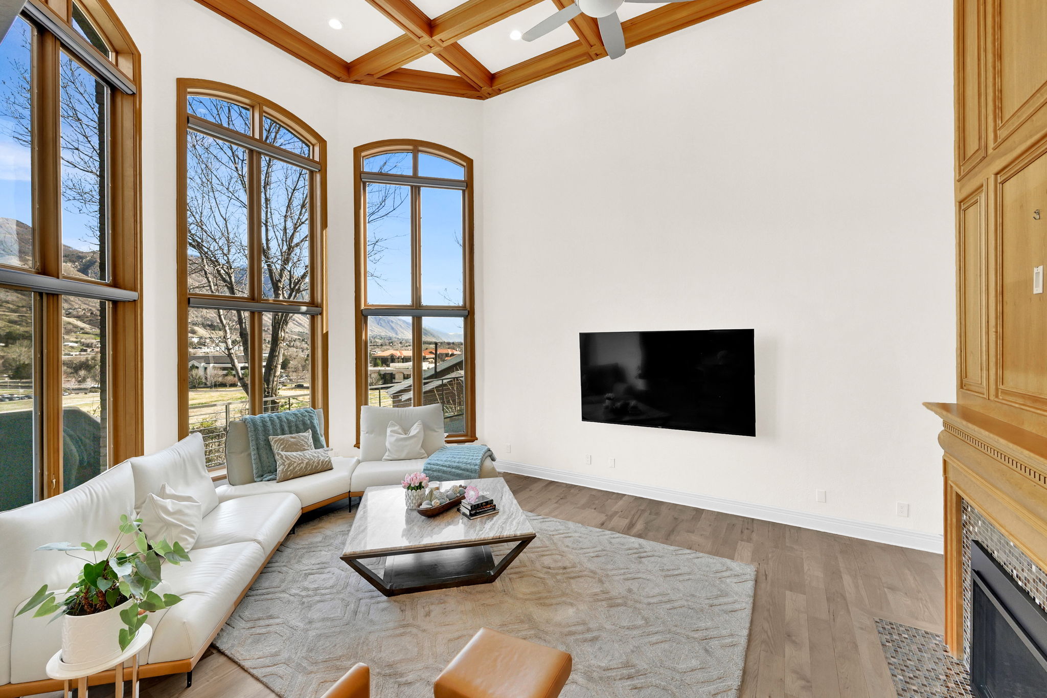 Mountain-facing living room with tall windows, warm wood ceiling detail, and fireplace