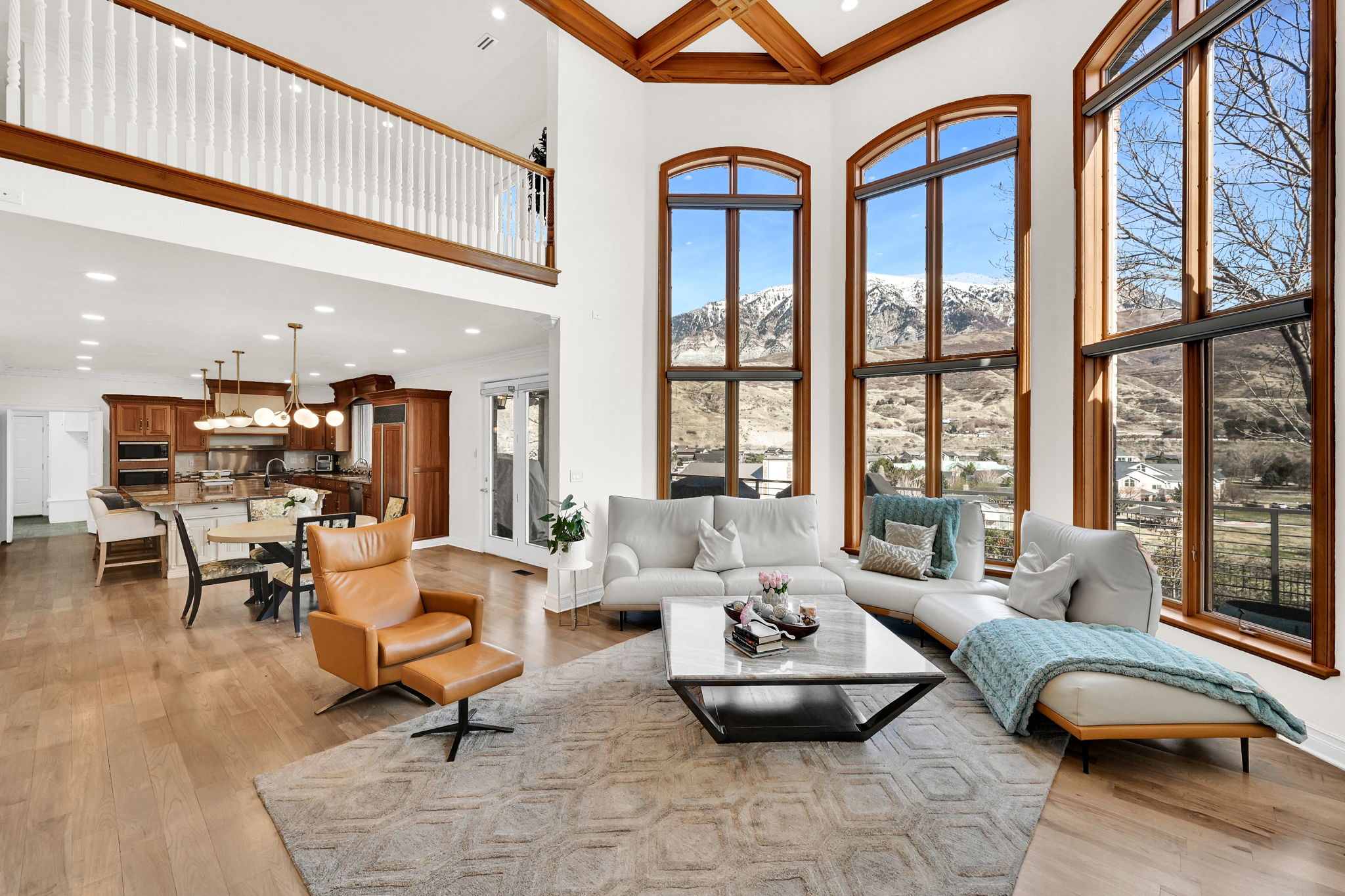 Grand great room with mountain-facing windows, warm wood fireplace surround, and open kitchen beyond